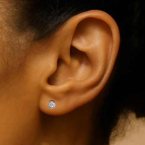 Close-up of an ear wearing a diamond stud earring with a blurred background