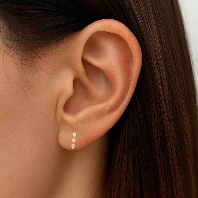 Close-up of an ear wearing a gold earring with a plain background