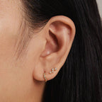 Close-up of an ear wearing gold earrings with a neutral background