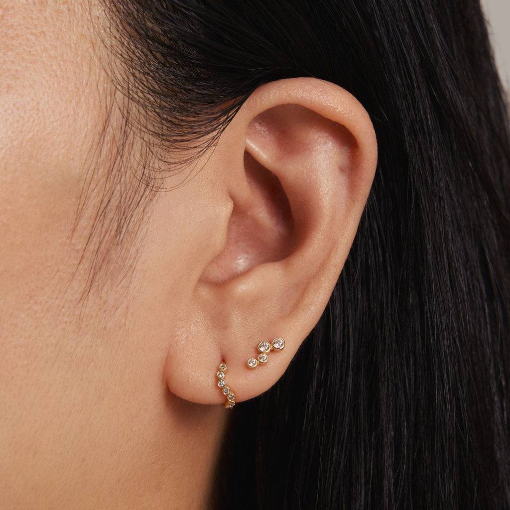 Close-up of an ear wearing gold earrings with a neutral background