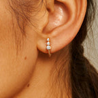 Close-up of an ear wearing a gold earring with three diamonds.