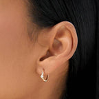 Close-up of an ear wearing a gold hoop earring with a small pearl.