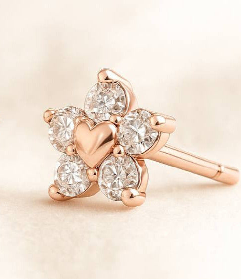 Rose gold earrings with heart design and clear gemstones on a beige background