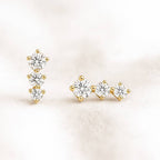 Gold earrings with clear gemstones on a light pink background
