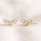 Pair of gold earrings with clear gemstones on a beige background