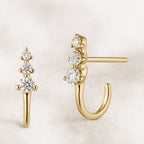 Gold earrings with clear gemstones on a light beige background