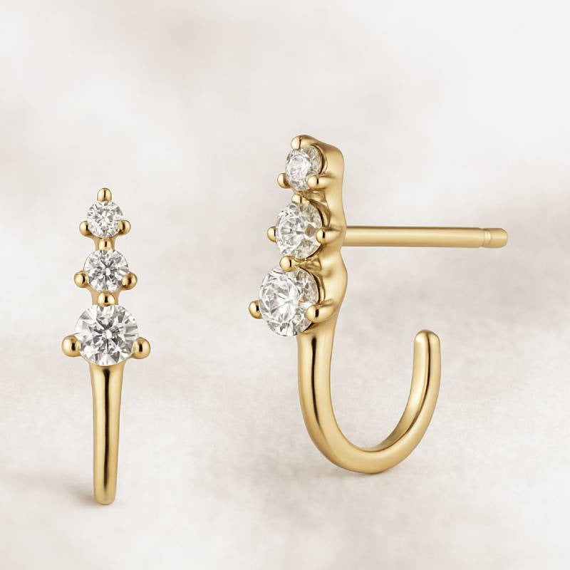 Gold earrings with clear gemstones on a light beige background