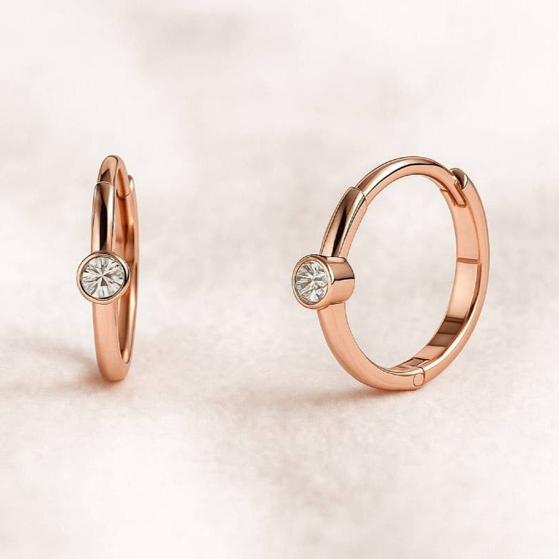 Rose gold hoop earrings with gemstones on a light pink background