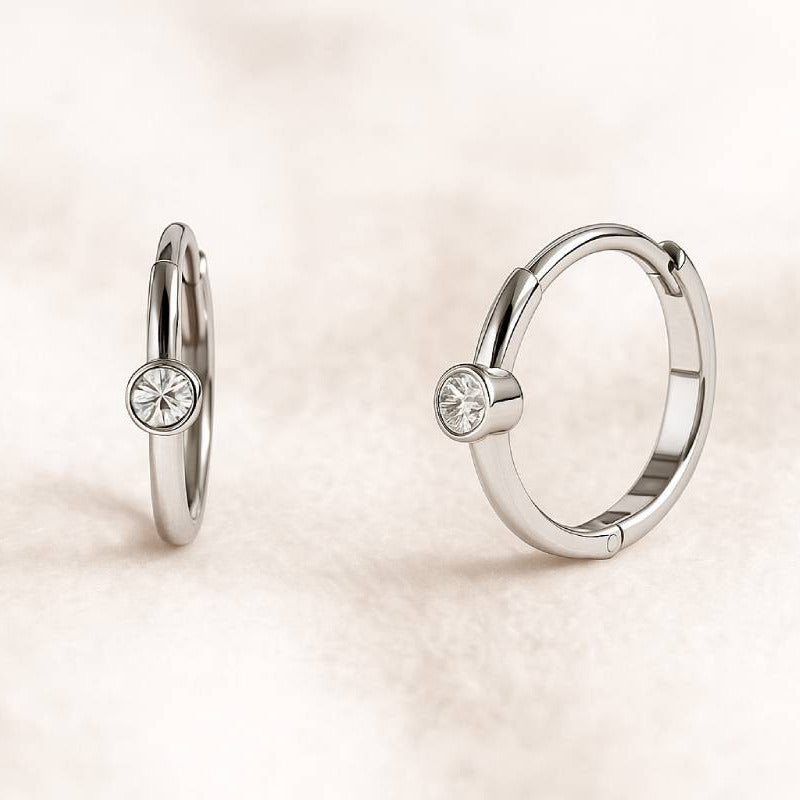 Pair of gold hoop earrings with small round gemstones on a light beige background