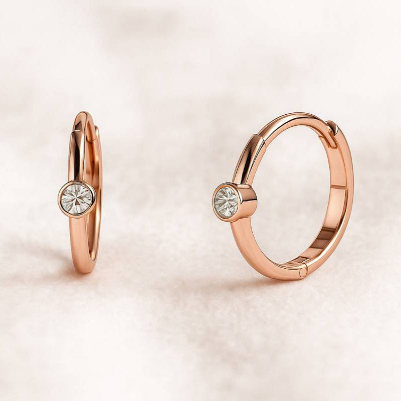 Rose gold hoop earrings with gemstones on a light pink background