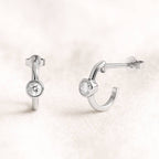 Pair of open hoop earrings with round gemstones on a light pink background