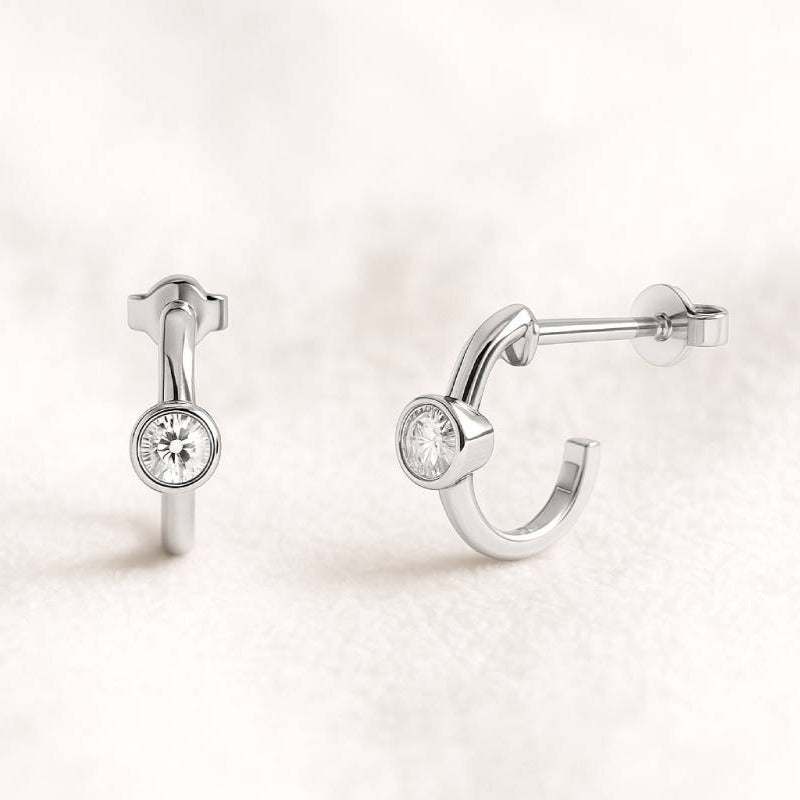 Pair of open hoop earrings with round gemstones on a light pink background