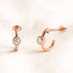 Rose gold hoop earrings with gemstones on a light pink background