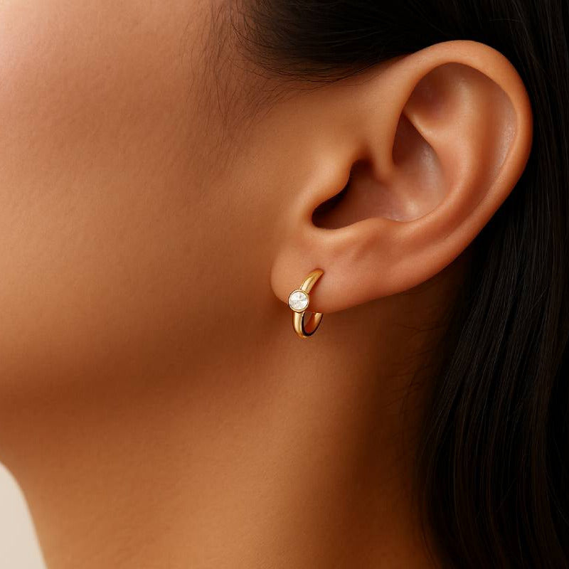 Close-up of a person wearing a gold earring with a pearl accent.