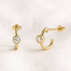 Gold hoop earrings with gemstones on a light pink background