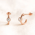 Rose gold hoop earrings with gemstones on a light pink background