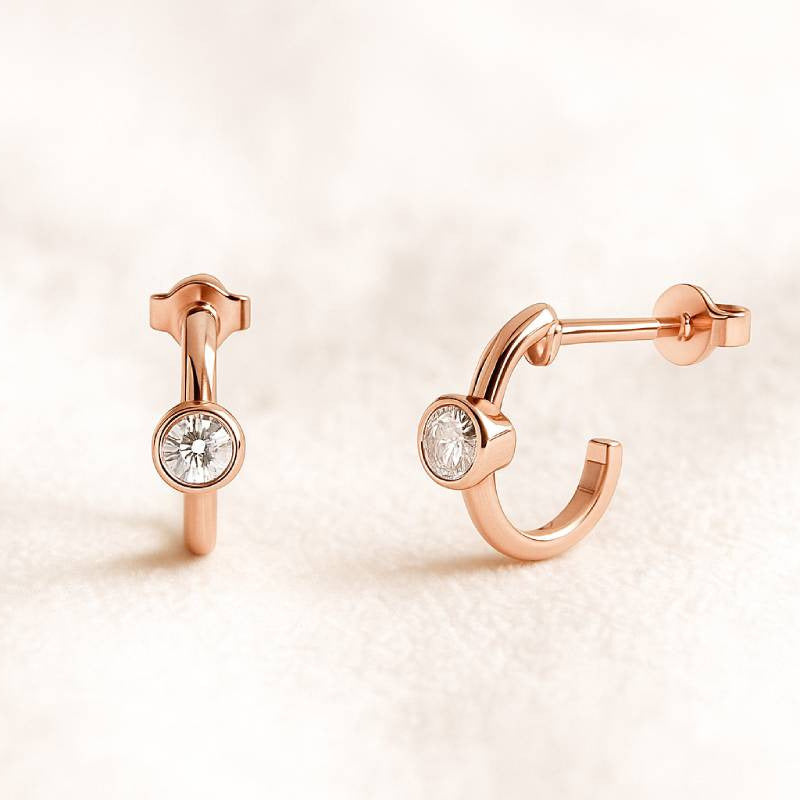 Rose gold hoop earrings with gemstones on a light pink background