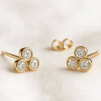 Gold earrings with three circular gemstones on a light background