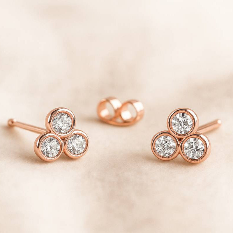 Rose gold earrings with diamond-like stones on a beige background