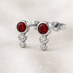 Gold earrings with red gemstones on a light background