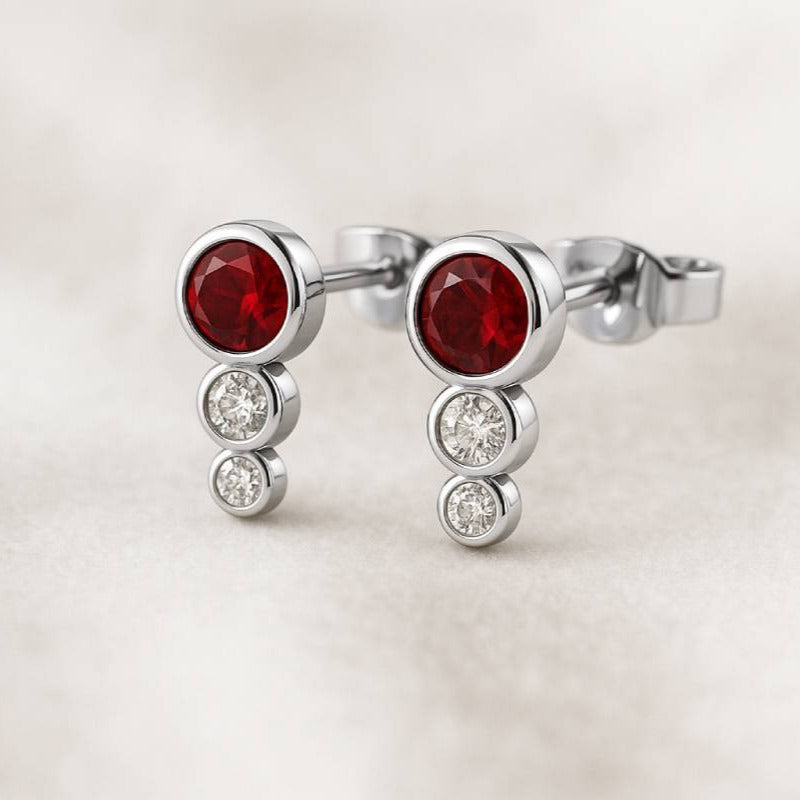 Gold earrings with red gemstones on a light background