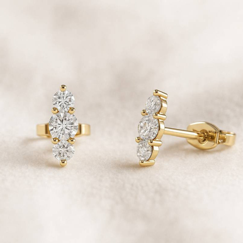 Gold earrings with clear gemstones on a beige background