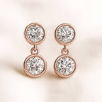Rose gold earrings with clear gemstones on a light pink background