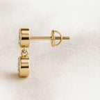 Gold earrings with a clear gemstone on a beige background