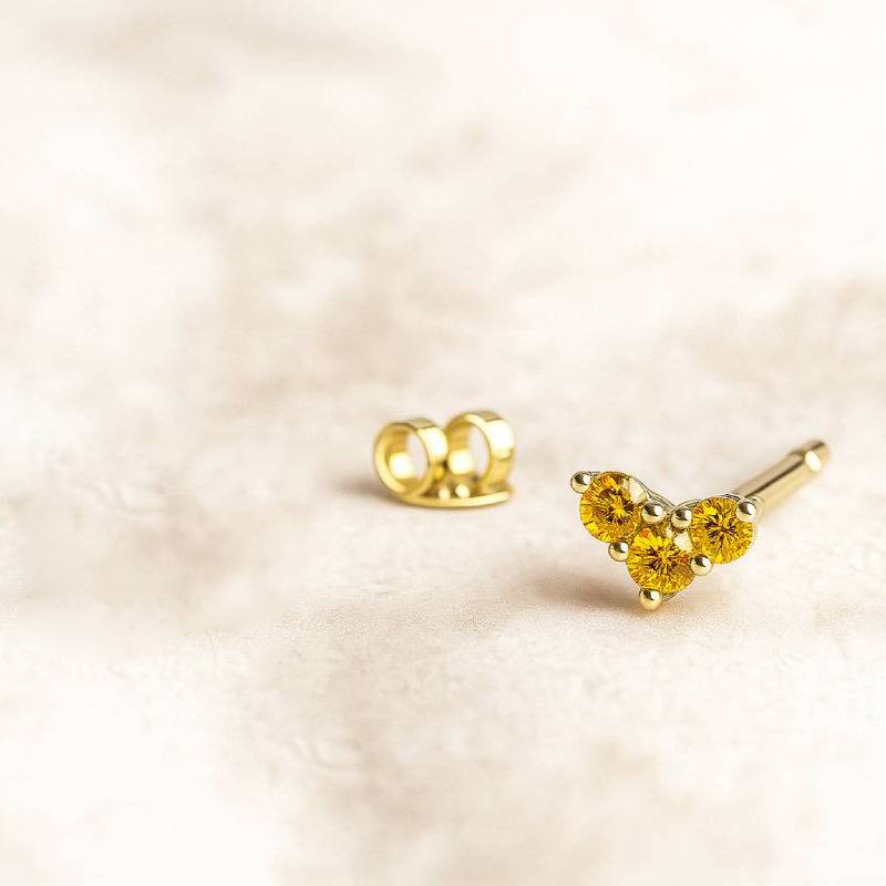 Gold earring with yellow gemstones on a soft beige background