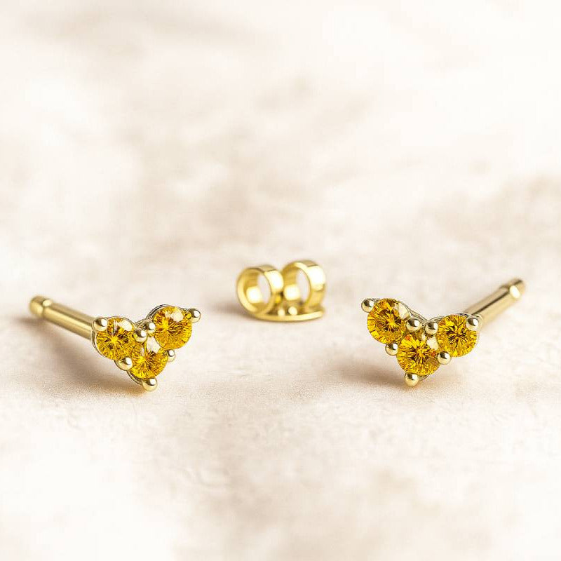 Set of gold earrings with yellow sapphire gemstones on a beige background