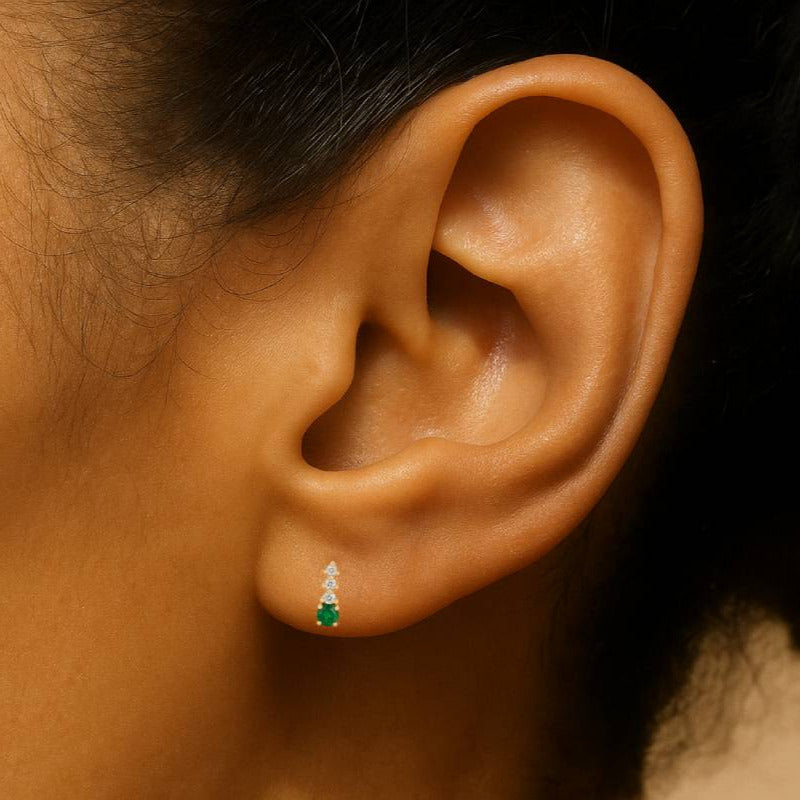 Close-up of an ear wearing a green emerald gemstone earring with a blurred background