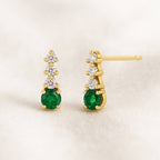 Gold earrings with green emerald gemstones on a beige background