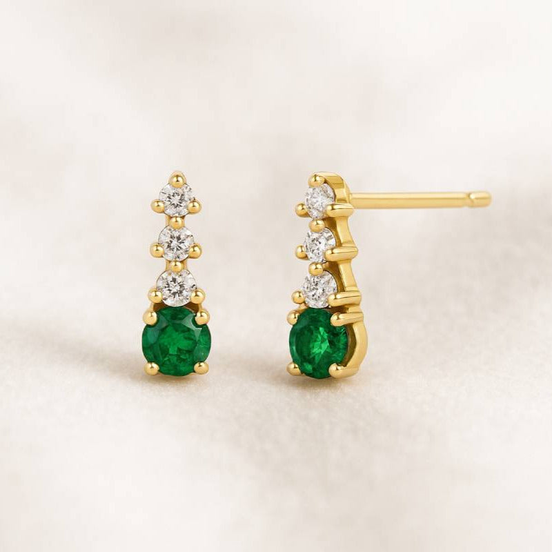 Gold earrings with green emerald gemstones on a beige background