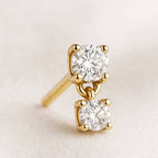 Gold earrings with clear gemstones on a light beige background