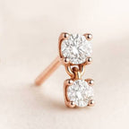 Rose gold earrings with two clear gemstones on a beige background