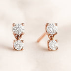 Rose gold earrings with clear diamonds on a light pink background