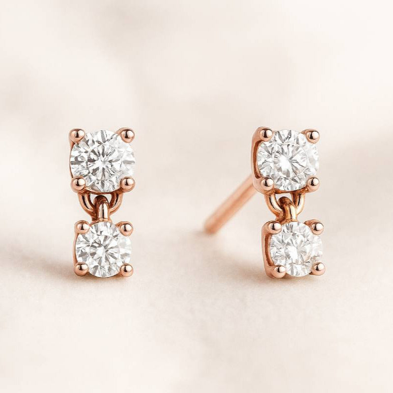 Rose gold earrings with clear diamonds on a light pink background
