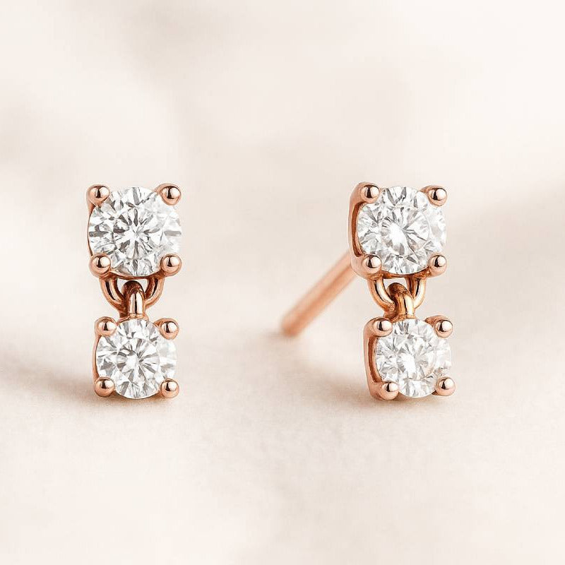 Rose gold earrings with clear diamonds on a light pink background