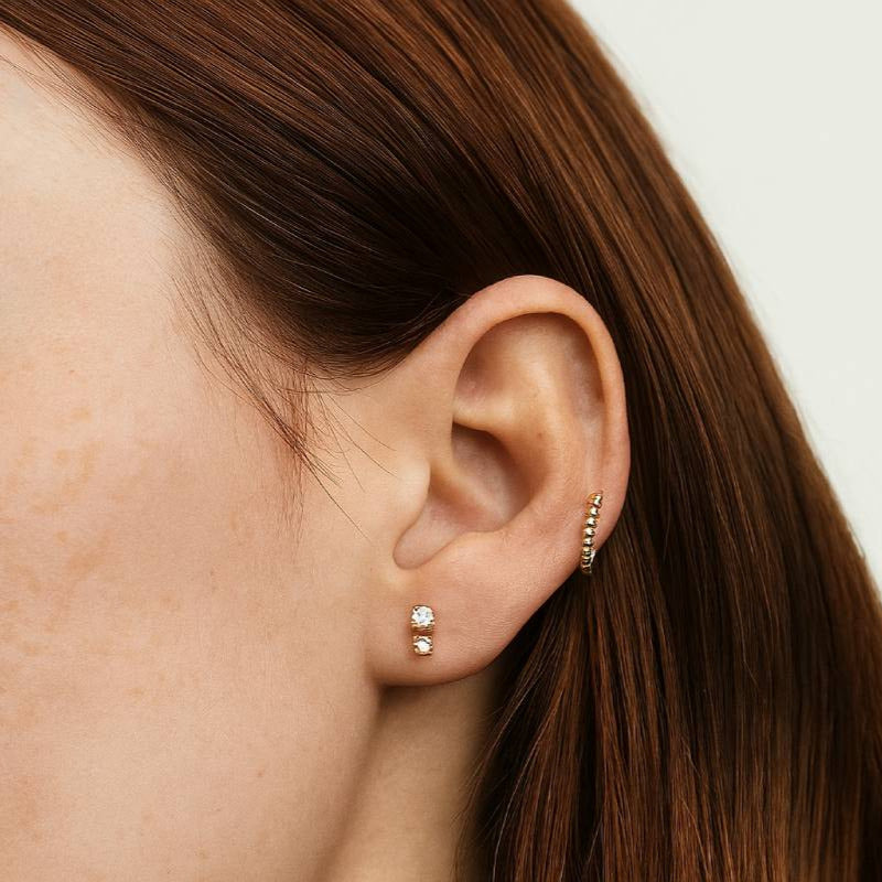 Close-up of a person wearing gold hoop earrings with a neutral background