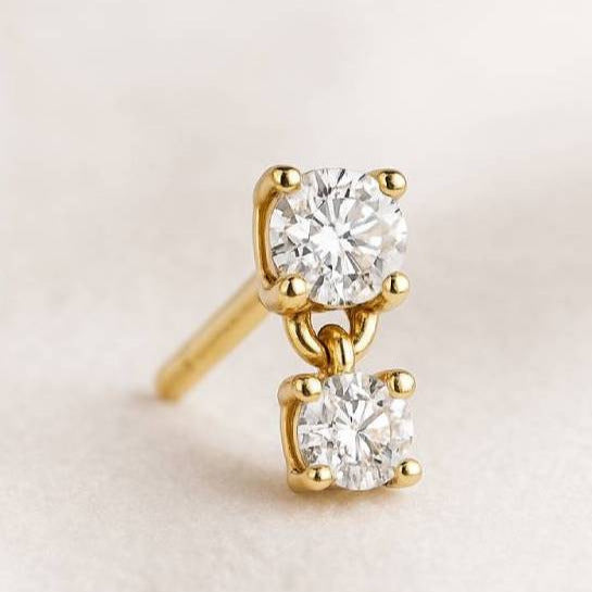 Gold earrings with clear gemstones on a light beige background