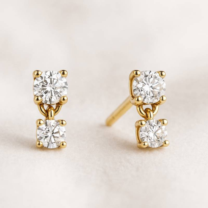 Gold earrings with clear diamonds on a light beige background