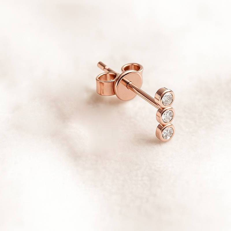 Rose gold earring with three clear gemstones on a light background