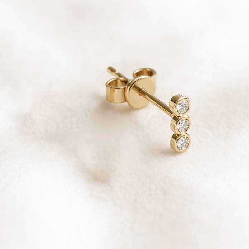 Gold earring with three diamonds on a light background