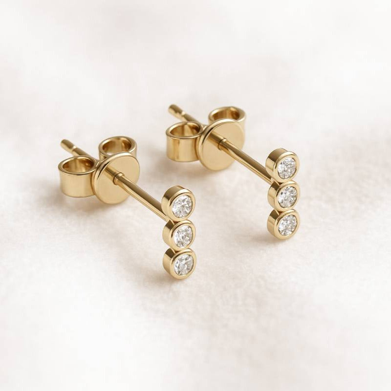 Gold stud earrings with diamonds on a light pink background