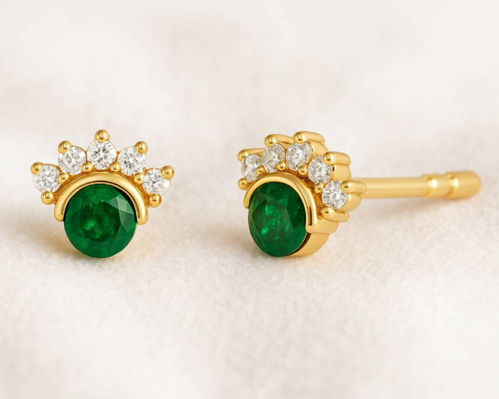 Gold earrings with green gemstones on a beige background