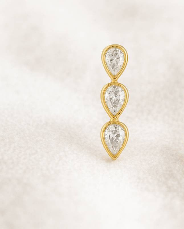 Gold earrings with three clear gemstones on a light beige background