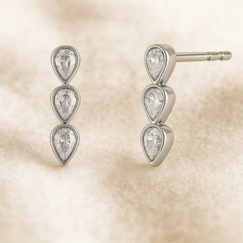Pair of silver teardrop earrings on a beige textured background