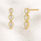 Gold earrings with clear gemstones on a light beige background