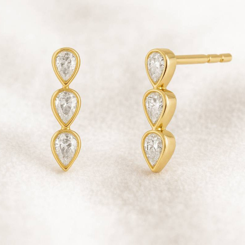Gold earrings with clear gemstones on a light beige background