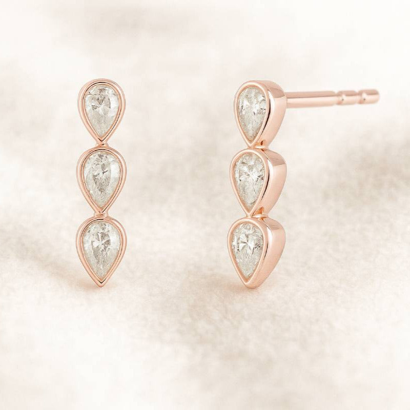 Rose gold earrings with clear gemstones on a soft beige background